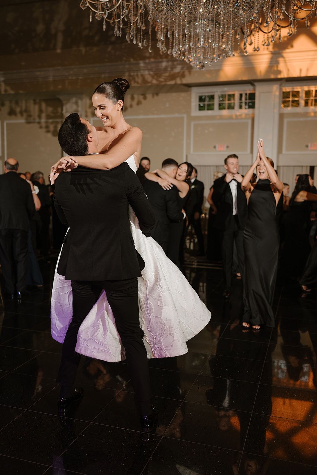 Groom lifting his laughing bride into the air on the crowded dance floor during the reception.
